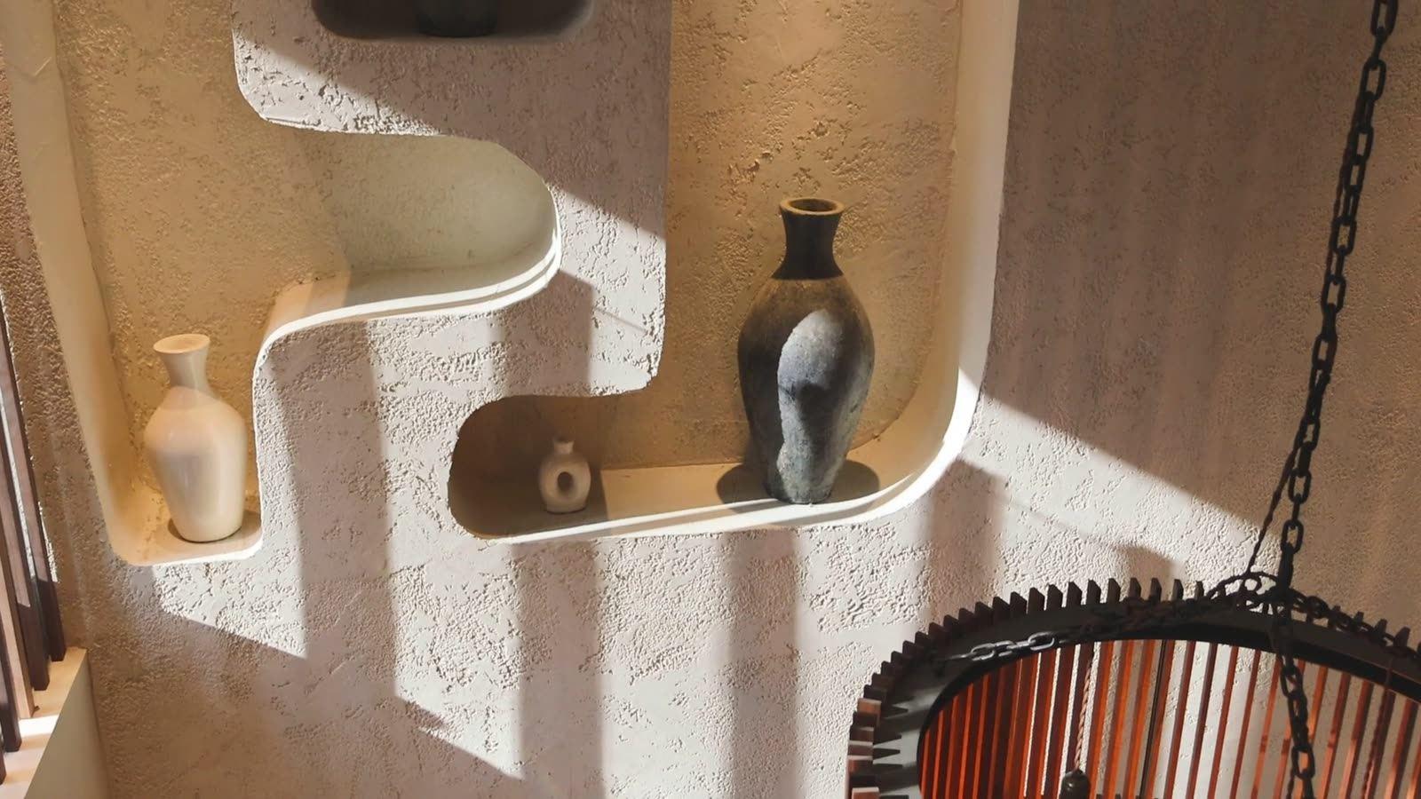 Sunlight moving across a textured plaster wall with sculpted display niches