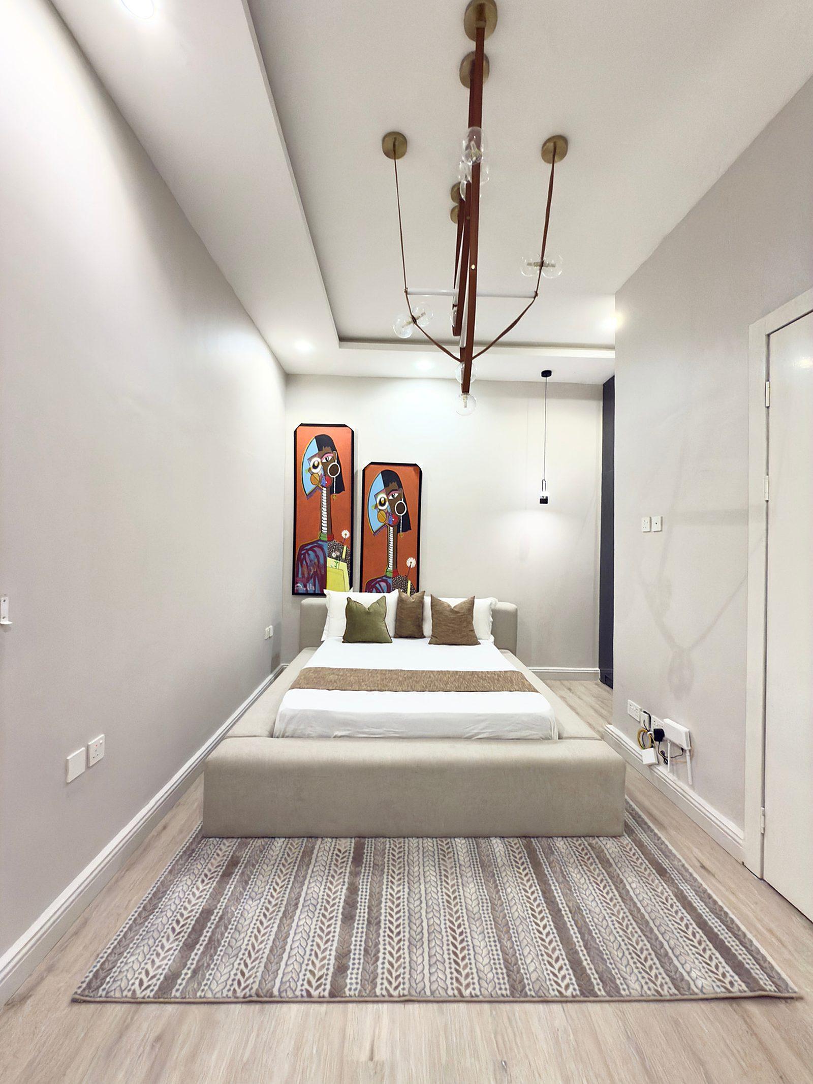Bedroom with a low upholstered bed, striped rug and a sculptural pendant light